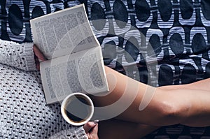 Detail of young woman and sun light. Woman keep a coffee cup and read a book.