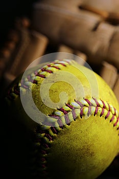 Closeup of a used, yellow softball resting in front of a brown glove.