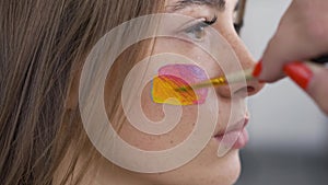 Detailed portrait of a young beautiful girl. Artist painting multicolor icon on the girl`s face using small soft brush