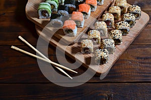 A detailed shot of a set of Japanese sushi rolls and a device for their use chopsticks, which are located on a wooden cutting b