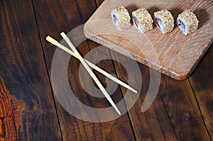 A detailed shot of a set of Japanese sushi rolls and a device for their use chopsticks, which are located on a wooden cutting b