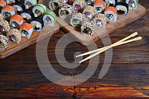 A detailed shot of a set of Japanese sushi rolls and a device for their use chopsticks, which are located on a wooden cutting b