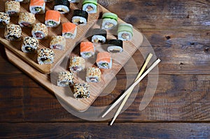 A detailed shot of a set of Japanese sushi rolls and a device for their use chopsticks, which are located on a wooden cutting b