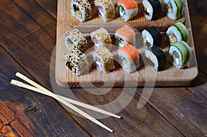 A detailed shot of a set of Japanese sushi rolls and a device for their use chopsticks, which are located on a wooden cutting b
