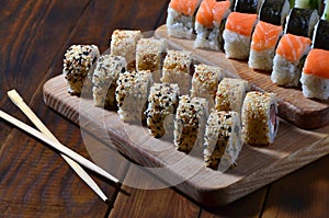 A detailed shot of a set of Japanese sushi rolls and a device for their use chopsticks, which are located on a wooden cutting b