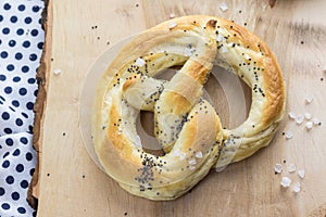 Detailed top view on a Pretzel with salt and poppy seeds on a wooden board
