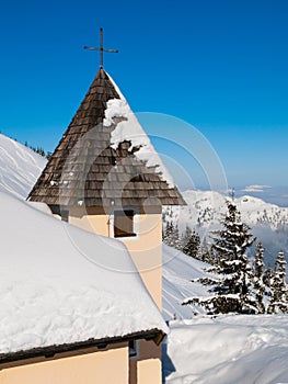 Detailed view of rural mountain church tower with cross on the top in snowy winter alpine landscape