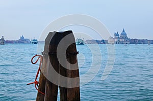 Detailed view of typical wooden pillars with rusty chain around and red rope for mooring nautical vessels in canal of Venice.