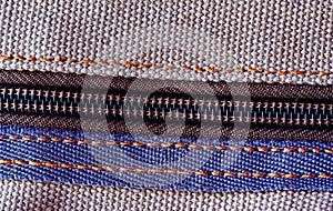 Detailed view of a zipper on brown textured fabric, highlighting the stitches