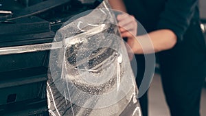Detailer worker smoothes PPF or Paint Protection Film on Car Headlight with working tool. Polymer protective outer photo