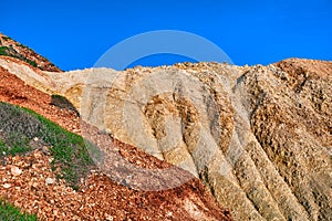 Details of the beautifully coloured cliffs on sunny day, clear blue sky. Yellow and red stone weathered slopes of Agios