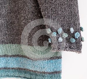 Details of blue, green and light grey hand knitted sweater with different textures including bobbles and ribbing.