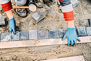 details of construction worker laying granite cobblestone on road pavement