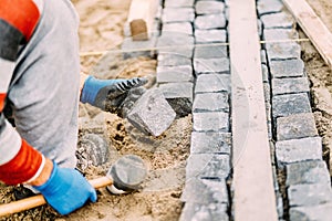 Details of construction works with industrial worker placing granite cobblestone blocks on path or alley