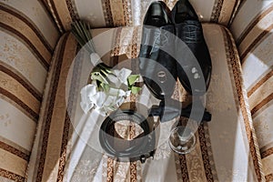 Details of the groom on the chair. Black velor boots, gold wedding rings, men's perfume, cufflinks