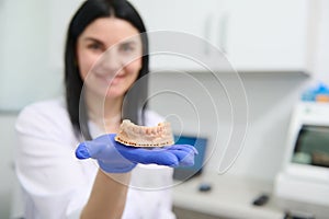Details: gypsum mold of the human lower jaw in the hand of a blurred smiling female dentist, dental technician.
