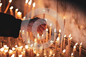 Details with the hands of an old woman lighting a candle inside a christian orthodox church in Romania