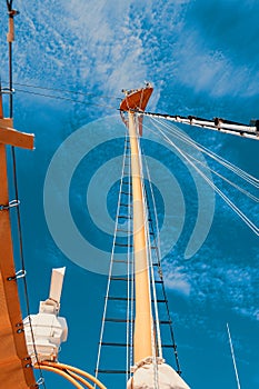 Details of a historic wooden sailboat against a cloudless sky. A pulley with the ropes of a classic sailing boat and a