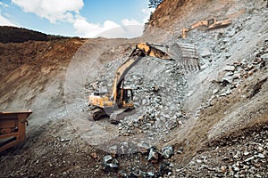 details of industrial track type excavator digging and loading ore in a dumper truck at a quarry