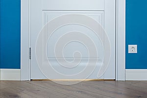 Details in the interior. Laminated parquet floors immitating oak texture, white baseboard, white door.