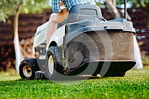 Details of landscaping and gardening. Worker riding industrial lawnmower