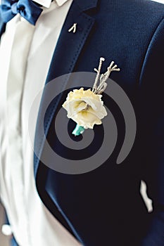 Details of male wedding clothes. Beautiful boutonniere pinned on man in blue suit, white shirt and blue bow tie.