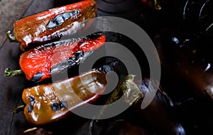 Details with roasted red paprikas and eggplants on top of an outdoors metal stove with wood fire