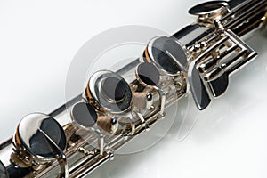 A silver bass flute lying on a white reflective surface