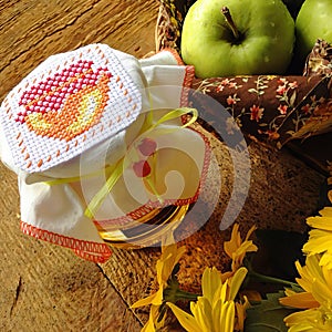 Details of a still life, a jar of honey covered with an embroidered towel and a basket of green apples. AI-generated item