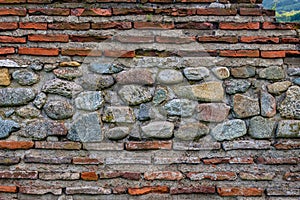 Details and texture of ancient Roman wall made of red bricks and colorful stones.