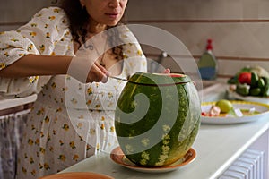 A watermelon and cropped view of a housewife cutting slices of ripe organic juicy berry, standing at the kitchen counter