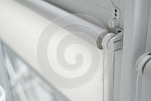 Details of white fabric roller blinds on the plastic window with wood texture in the living room.