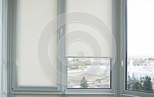 Details of white fabric roller blinds on the plastic window with wood texture in the living room.