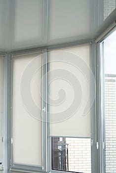 Details of white fabric roller blinds on the plastic window with wood texture in the living room.