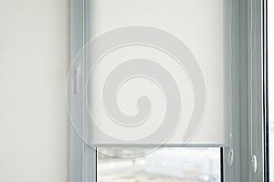 Details of white fabric roller blinds on the plastic window with wood texture in the living room.