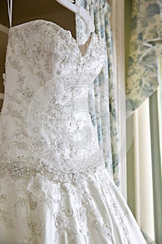 Details of a white wedding dress hanging in a room waiting for a bride