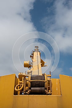 Details of a yellow industrial crane against blue cloud sky. Heave duty machinery for construction outdoor