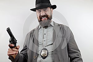 Detective with beard wearing hat and police badge holding gun with angry expression on face.