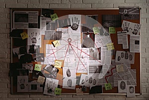 Detective board with fingerprints, photos, map and clues connected by red string on white brick wall