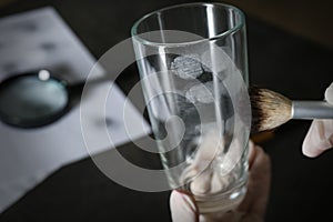 Detective taking fingerprints with brush from glass, closeup