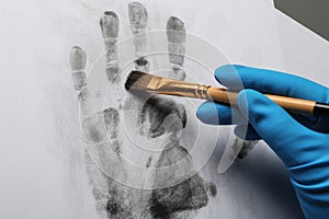 Detective taking fingerprints with brush from paper on grey