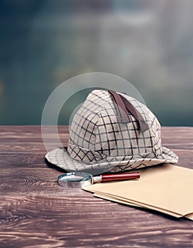 Detectiveâ€™s hat, magnifying glass, and papers on a wooden surface, set against a cloudy backdrop. A scene of mystery and