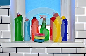 Detergent and sponge on the windowsill against the background of white ceramic tiles. Detergents bottles and kitchen sponges.