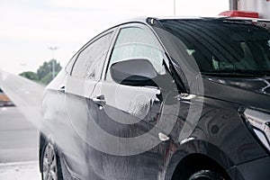 Detergent is washed off with water from the side of the gray car at the sink