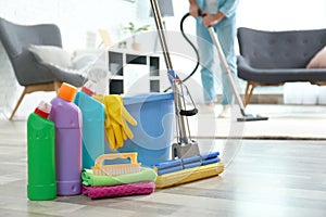 Detergents, bucket and mop on floor with janitor vacuuming carpet