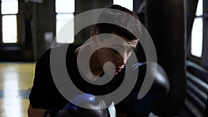 Determinated young boxer punching black bag in vintage stylized gym. Caucasian young man hitting the punching bag in