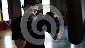 Determinated young boxer punching black bag in vintage stylized gym. Caucasian young man hitting the punching bag in