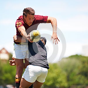 Determination keeps our game strong. a young rugby player executing a pass mid-tackle.