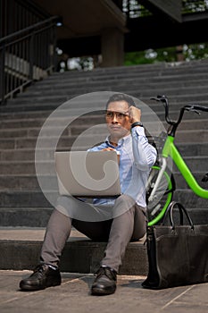 A determined Asian businessman sits on steps, working on a laptop, deep in thought