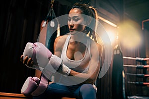 Determined Asian female Muay Thai boxer wraps her hand. Impetus